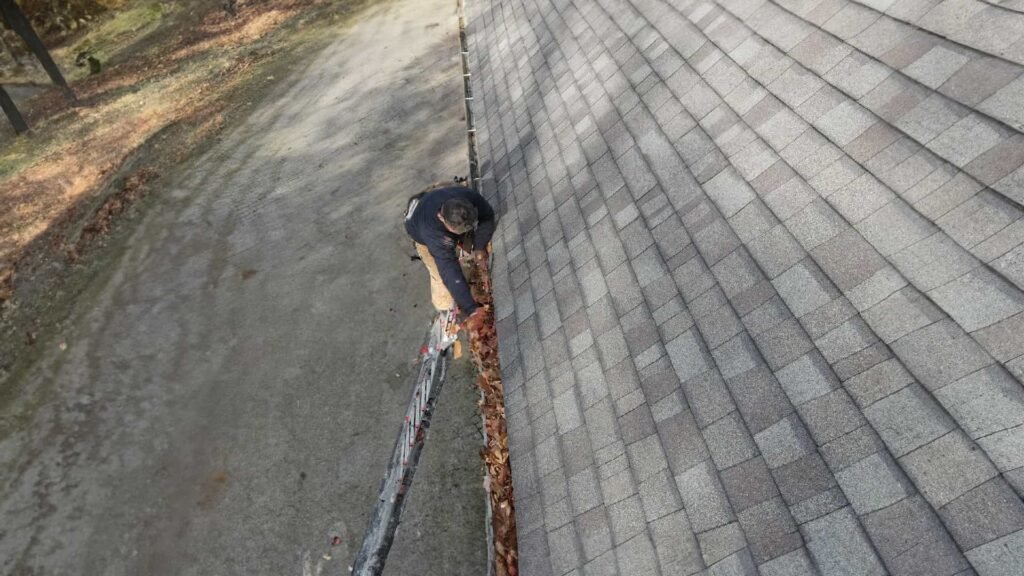 Worker cleaning leaves from a gutter on a residential roof